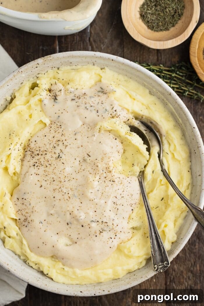 Creamy white gravy generously poured over a bowl of fluffy mashed potatoes, ready to be served as a comforting side dish.