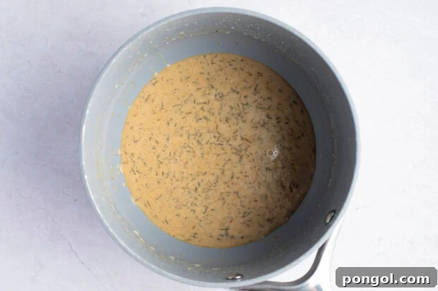 A mixture of melted butter and flour forming a pale roux in a saucepan, being whisked to combine.