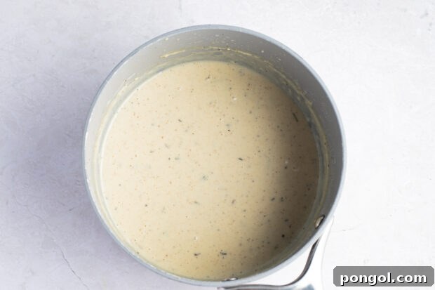 Smooth, creamy white gravy simmering in a medium saucepan, almost ready to serve.