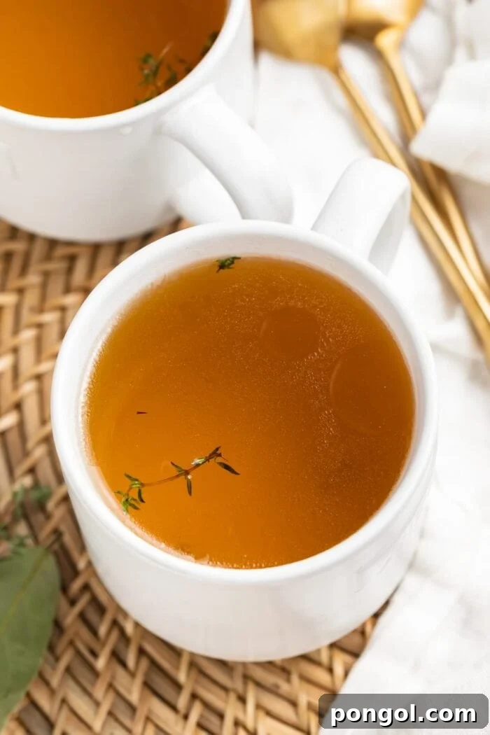 beef consommé in two mugs with fresh thyme on top