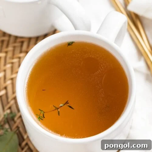 beef consommé in two mugs with fresh thyme on top