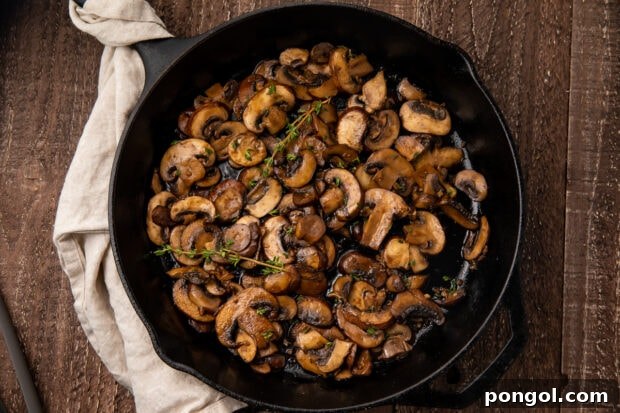 Finished sautéed mushrooms, perfectly cooked and garnished with fresh thyme, in a large skillet.