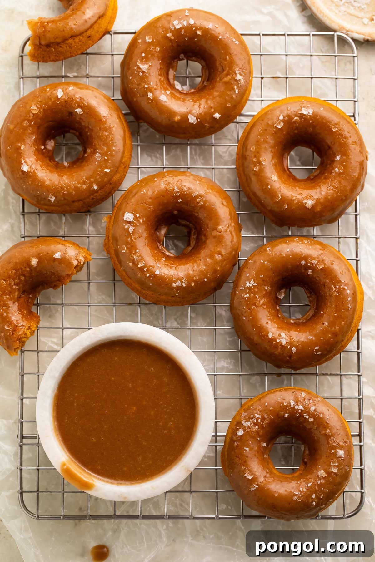 Overhead view of vegan pumpkin donuts on cooling rack with bowl of caramel sauce