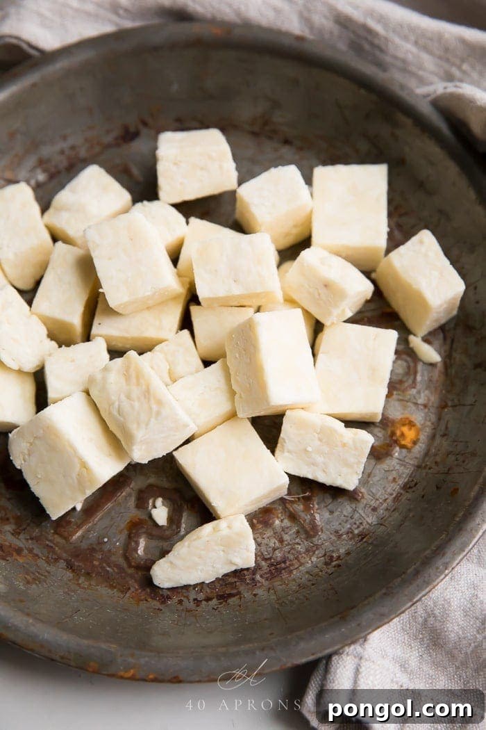 Cubes of freshly made paneer, a soft Indian cheese, arranged in a rustic metal dish, ready for cooking or serving. This homemade paneer is exceptionally creamy and melts beautifully, perfect for enhancing any Indian recipe. Experience the superior taste and texture that only fresh, handcrafted paneer can offer for your vegetarian Indian culinary adventures.