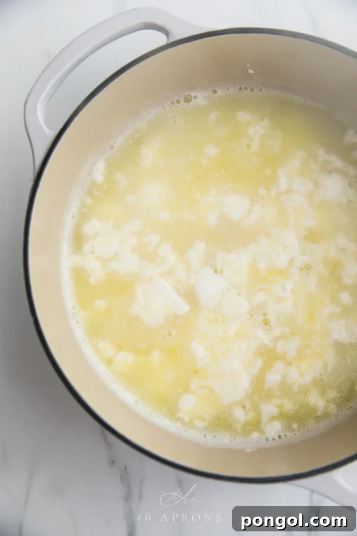 The contents of a pot showing milk that has perfectly separated into solid white curds and clear yellow whey after the addition of lemon juice. This visual clearly illustrates the successful first stage of making homemade Indian cheese, demonstrating the distinct curd formation.