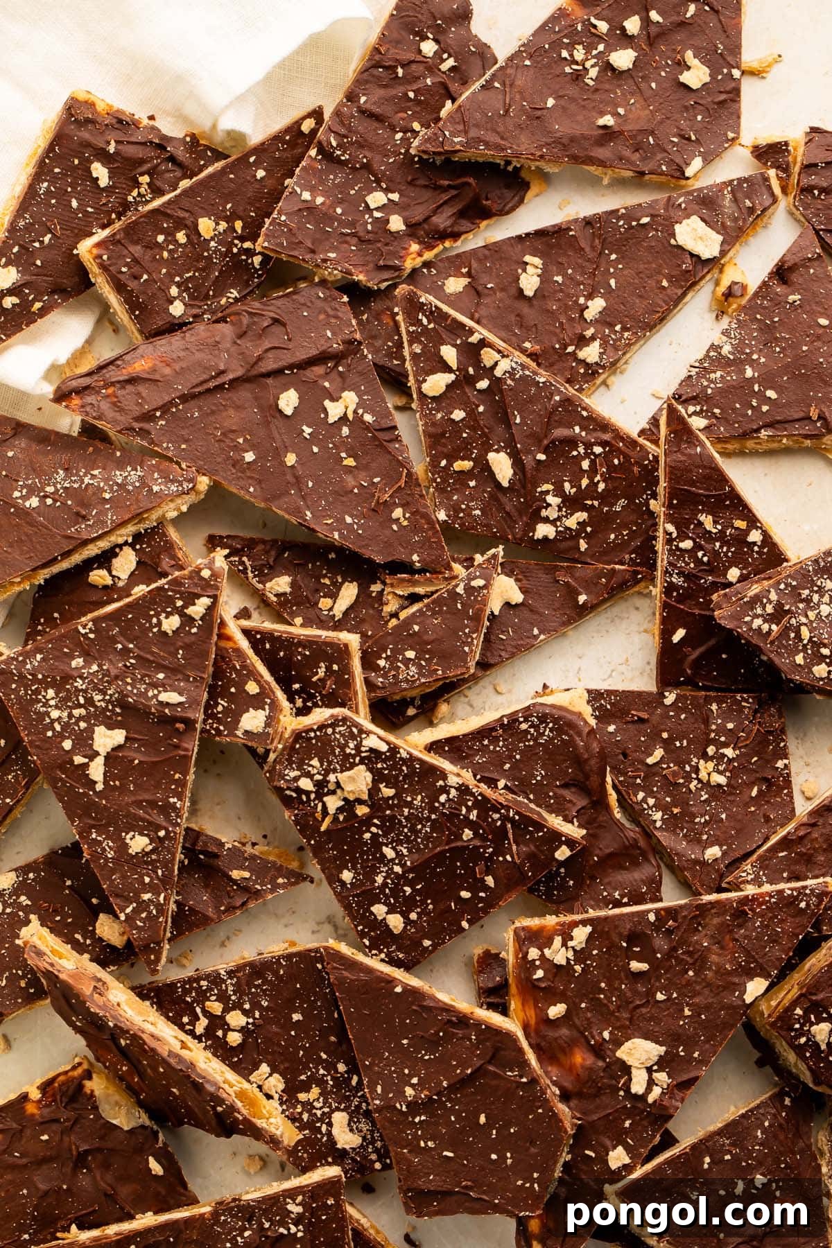 Broken pieces of saltine toffee in a pile on a piece of parchment paper, showcasing the multiple layers of cracker, caramel, and chocolate.
