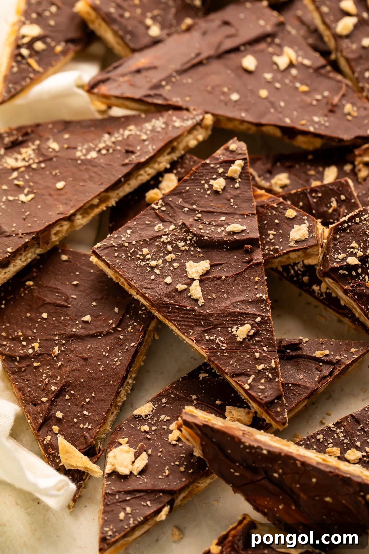 Various pieces of saltine toffee arranged on parchment paper, displaying the crunchy cracker base, rich caramel, and smooth chocolate layers.