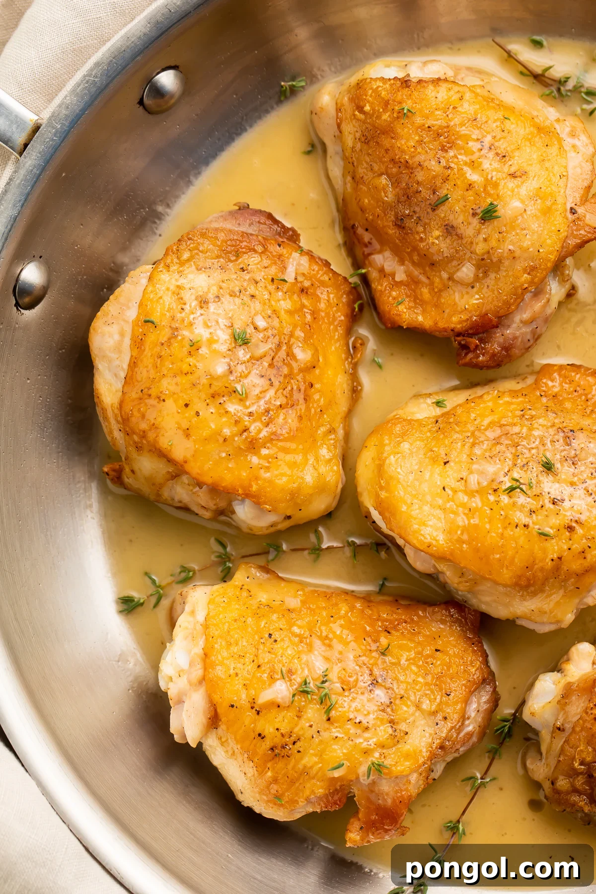 Pan-seared chicken thighs in a simple pan sauce, resting in a silver saucepan.
