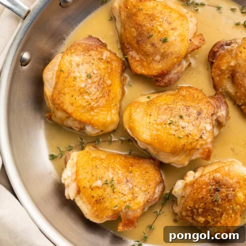 Pan-seared chicken thighs in a simple pan sauce, resting in a silver saucepan.
