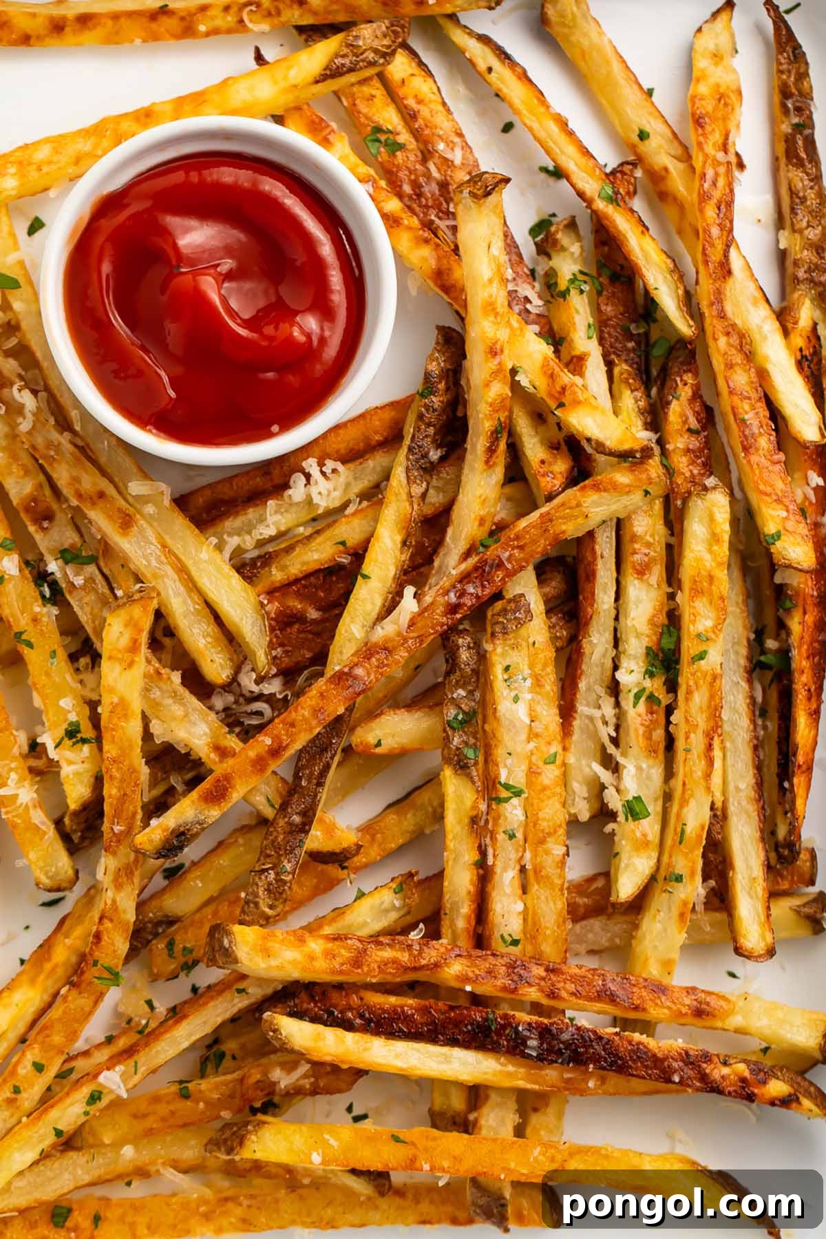 Crispy Parmesan truffle fries generously scattered across a sheet pan lined with parchment paper, positioned next to a small ramekin of classic ketchup for dipping.