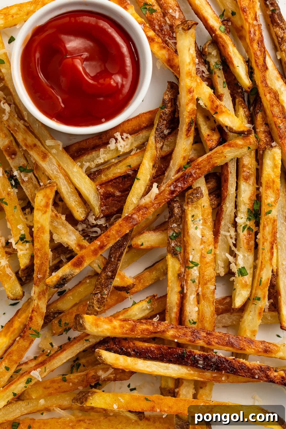 Close-up shot of crispy Parmesan truffle fries glistening with oil and cheese, next to a small ramekin of ketchup on a parchment-lined sheet pan.
