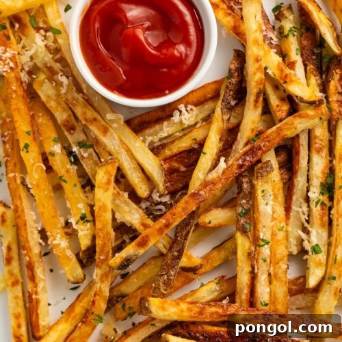 Crispy Parmesan truffle fries generously scattered across a sheet pan lined with parchment paper, positioned next to a small ramekin of classic ketchup for dipping.