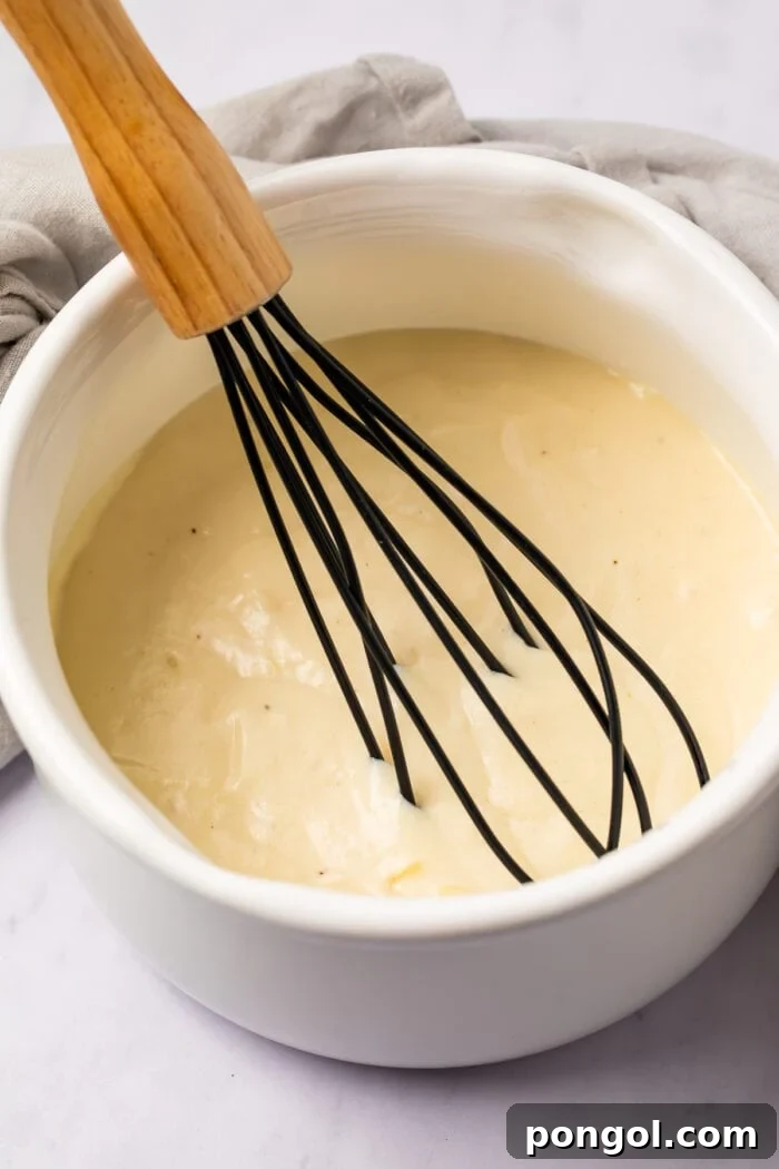 Whisk in a bowl with mornay sauce on a light surface