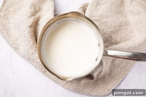 Hot milk in a small saucepan on a white surface with a neutral linen