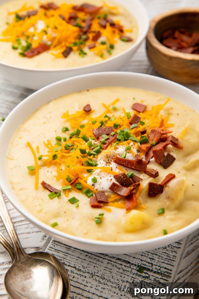 A side view of a bowl of vegan potato soup sitting on a table, garnished with fresh herbs and a swirl of vegan cream.