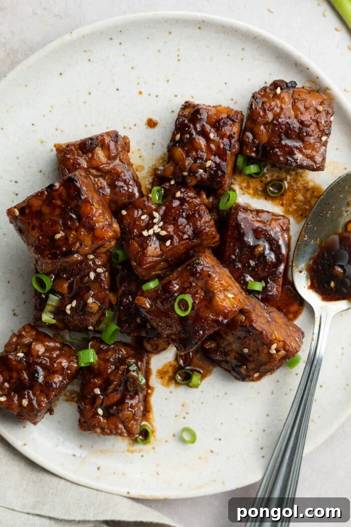Crispy, golden-brown tempeh pieces garnished with fresh scallions and sesame seeds on a white plate.