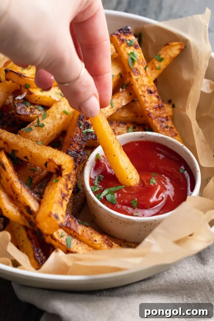 Crispy rutabaga fries being dipped in a dollop of ketchup