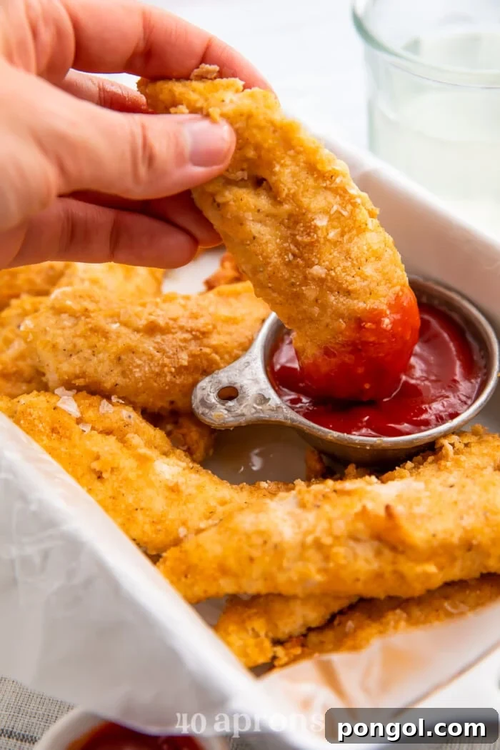 Whole30 chicken tenders surrounding a cup of ketchup while a hand dips a chicken tender into the ketchup