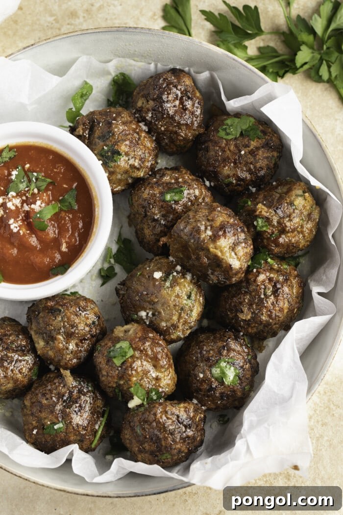 A plate of perfectly cooked air fryer meatballs, with a small ramekin of rich marinara sauce beside them, ready for dipping.