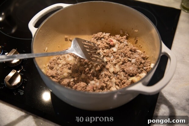 Ground meat and onions cooking in a saucepan, starting to brown.