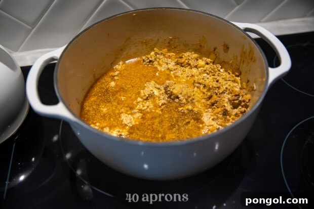 Taco seasoning being sprinkled over browned ground meat and onions in a pot.