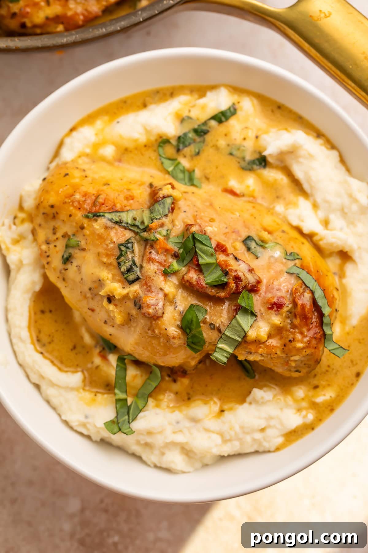 Single Whole30 marry me chicken breast on mashed cauliflower with creamy sauce and basil garnish.