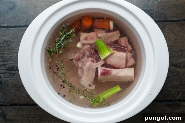 Raw bones in a crockpot with vegetables and herbs, ready for broth making.
