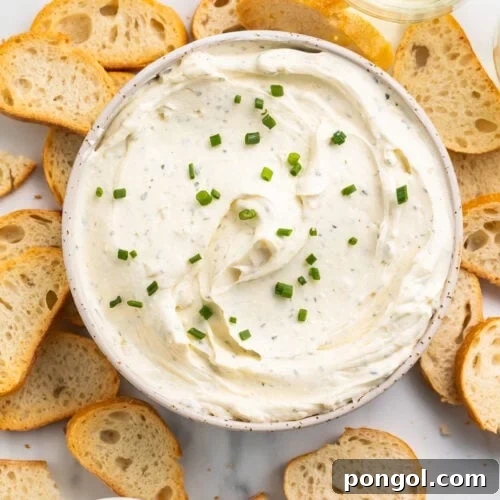An overhead view of a bowl filled with creamy homemade boursin cheese surrounded by crisp crostini.