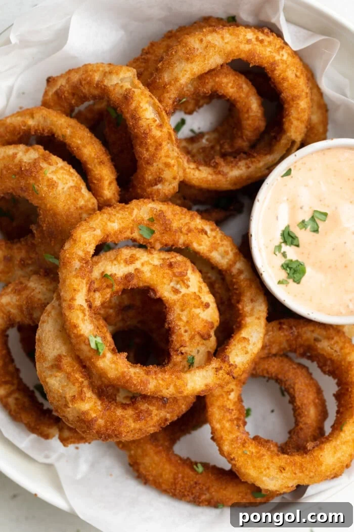 Crispy Air Fried Frozen Onion Rings with Bloomin' Onion Dip 2 Crispy frozen onion rings served in a bowl with a side of bloomin' onion dipping sauce, captured from an overhead perspective.