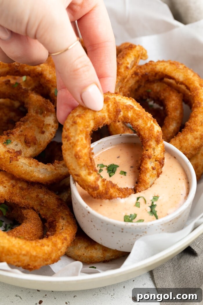 Crispy Air Fried Frozen Onion Rings with Bloomin' Onion Dip 3 A single crispy air-fried frozen onion ring being dipped into a small bowl of bloomin' onion sauce.