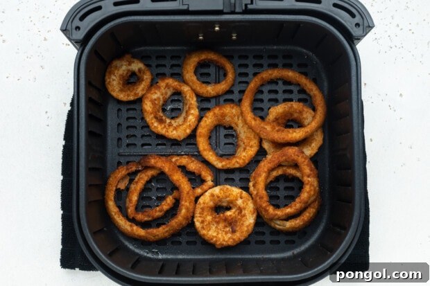 Air fryer basket filled with frozen onion rings cooking, with a slight blur indicating movement from shaking.