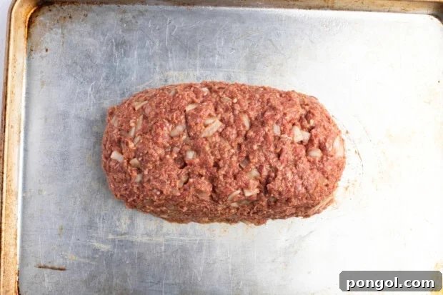 Loaf-shaped, uncooked meatloaf on baking sheet