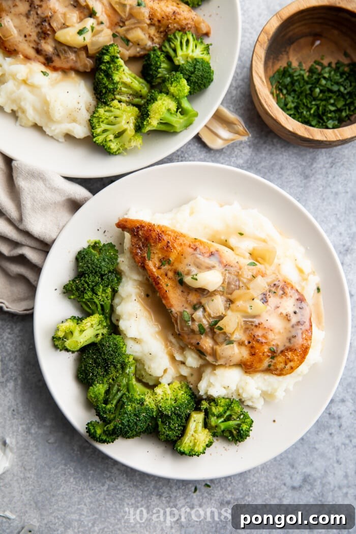 Whole30 creamy garlic chicken served on a white plate with a side of creamy mashed potatoes and vibrant green broccoli florets.