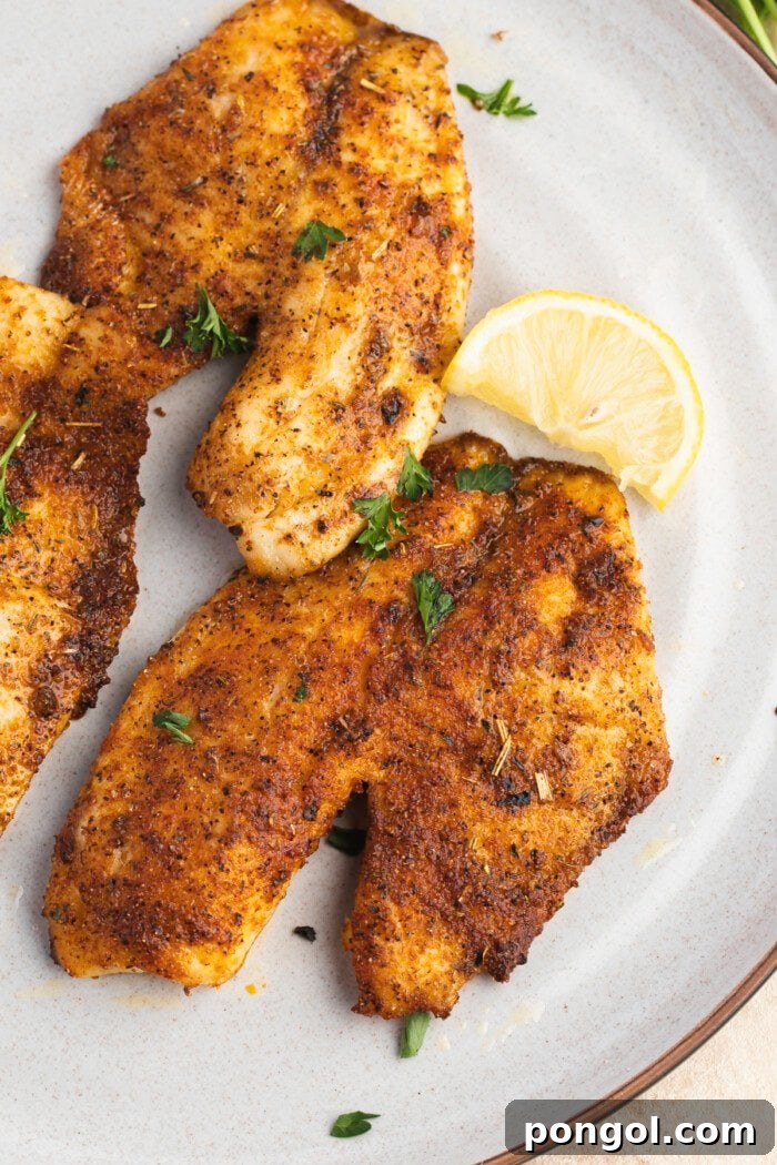 Golden Air Fryer Tilapia 3 Overhead view of perfectly air-fried tilapia fillets on a white plate, ready to be served, showcasing their golden-brown crust.