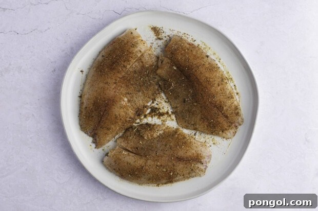 Golden Air Fryer Tilapia 7 Seasoned tilapia fillets on white plate.