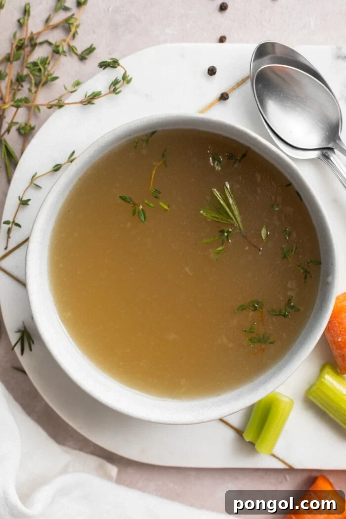 A bowl of rich bone broth with fresh carrots, celery, thyme, and black peppercorns artfully arranged on the side, highlighting its natural goodness.