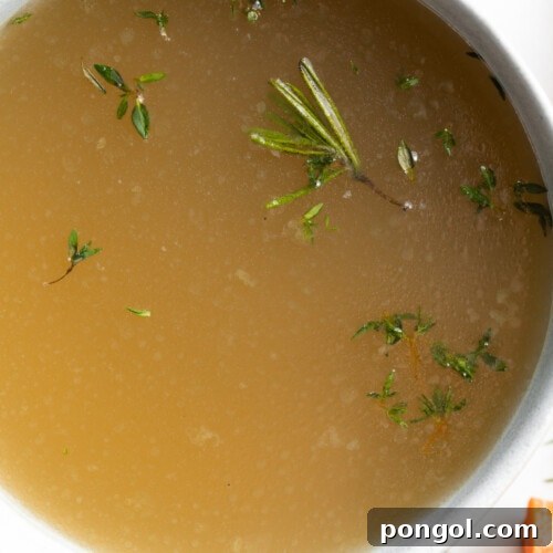 Close-up overhead image of bone broth in a bowl with fresh herbs on top, showcasing its rich texture and inviting aroma.