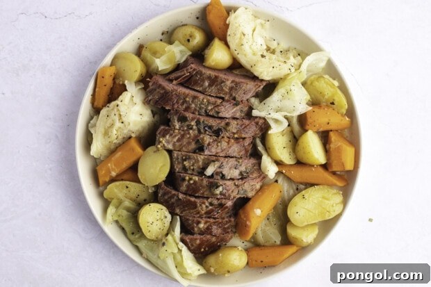 Sliced corned beef brisket with potatoes, carrots, and cabbage on white platter, ready to serve.