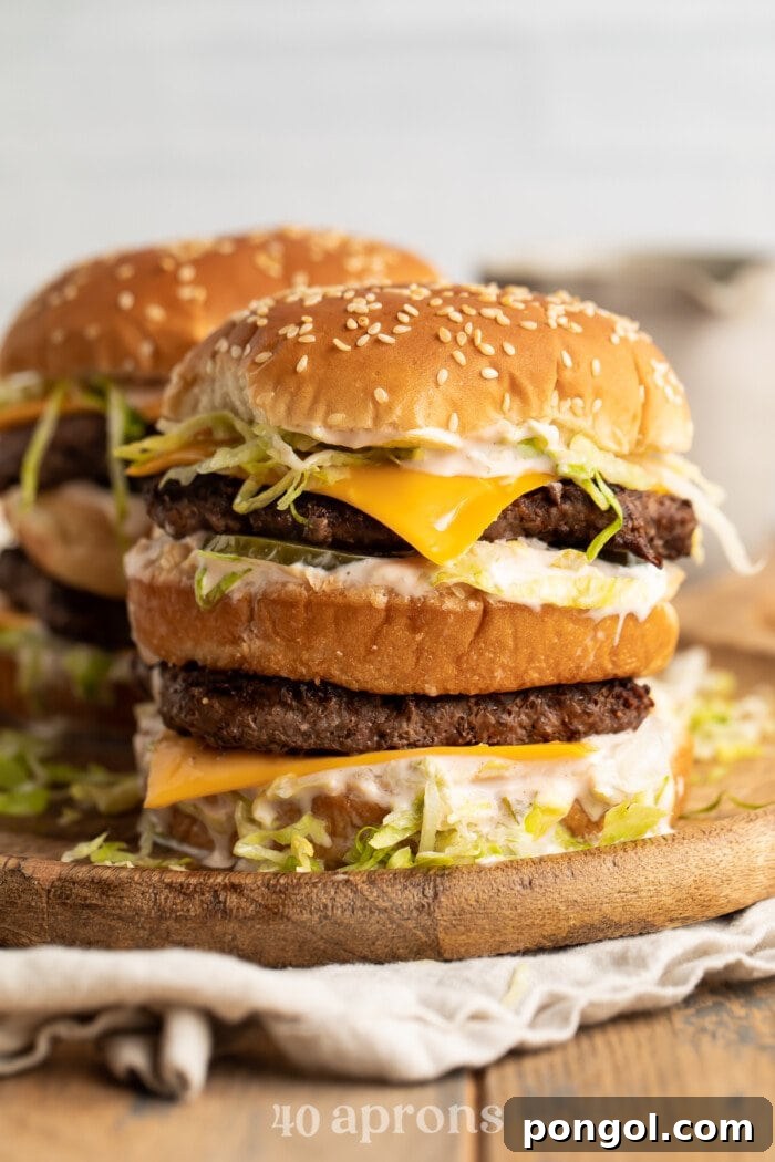 A stack of keto big macs on a wooden cutting board, showcasing the layers of patties, cheese, lettuce, and special sauce.