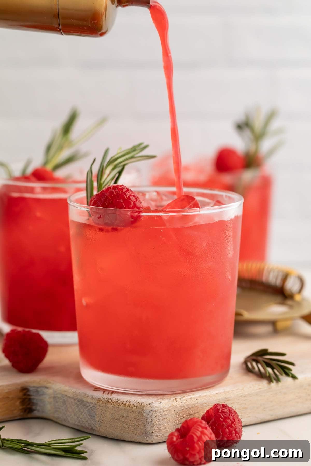 Rosemary Raspberry Elixirs 3 A raspberry cocktail being poured from a cocktail shaker into a glass, showing the mixing process.