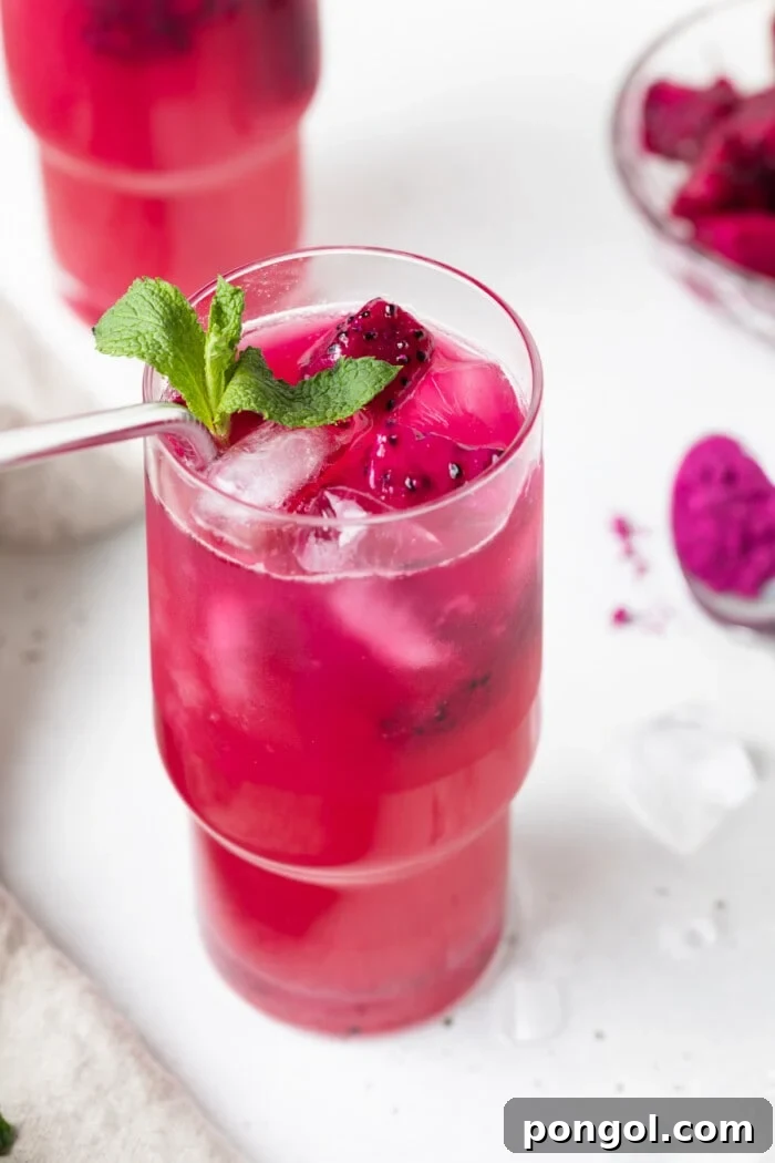 Two glasses of vibrant mango dragon fruit refreshers, garnished with fresh mint leaves, ready to be enjoyed on a bright day.