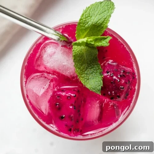 Overhead view of a glass filled with a mango dragon fruit refresher, with ice and fruit pieces.