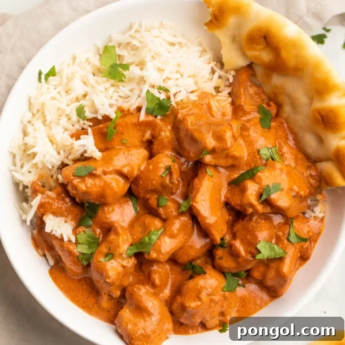 Zoomed out photo of butter chicken in a creamy red-orange sauce plated next to white rice and naan.