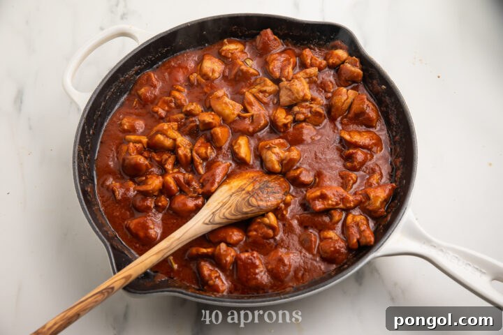 Velvet Butter Chicken 6 Chicken thighs with spiced butter, tomato sauce, and a wooden spoon in a large wok.