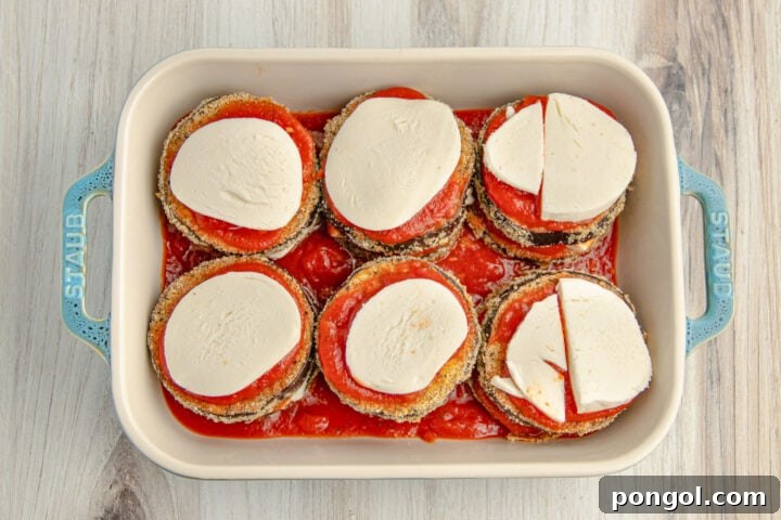 Unbaked keto eggplant parmesan topped with discs of mozzarella in a 9x13 baking dish.