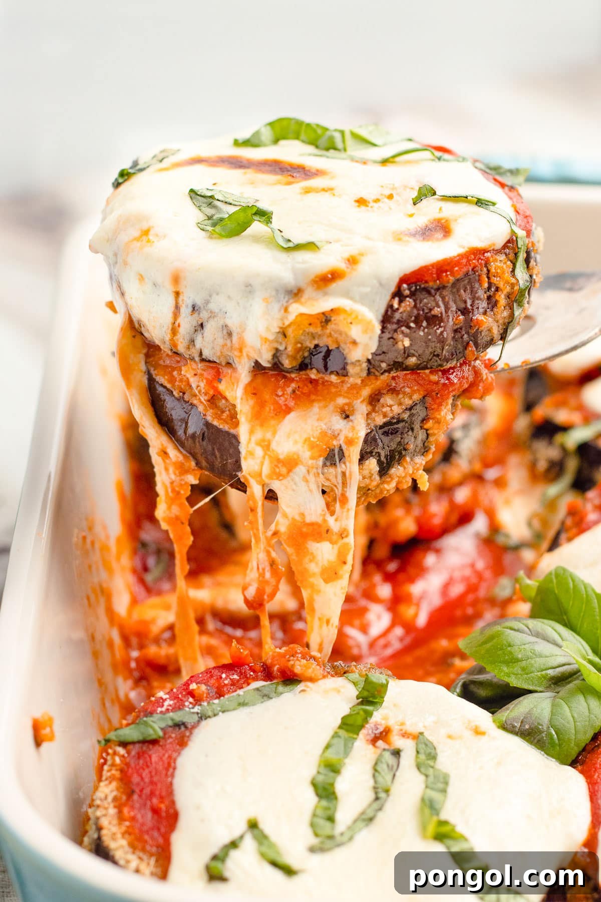 Keto eggplant parmesan slices being lifted out of a baking dish.