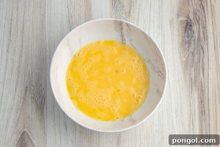 Egg wash in shallow bowl on a light neutral countertop.