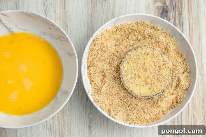 Breaded eggplant disc in a shallow bowl of keto breading.