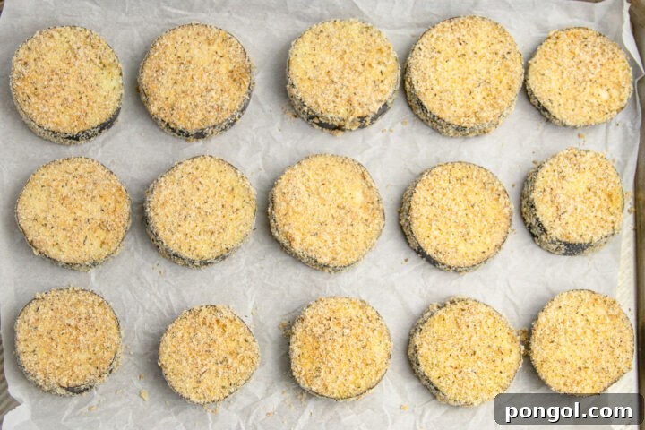 Breaded eggplant discs on a baking sheet lined with parchment paper.