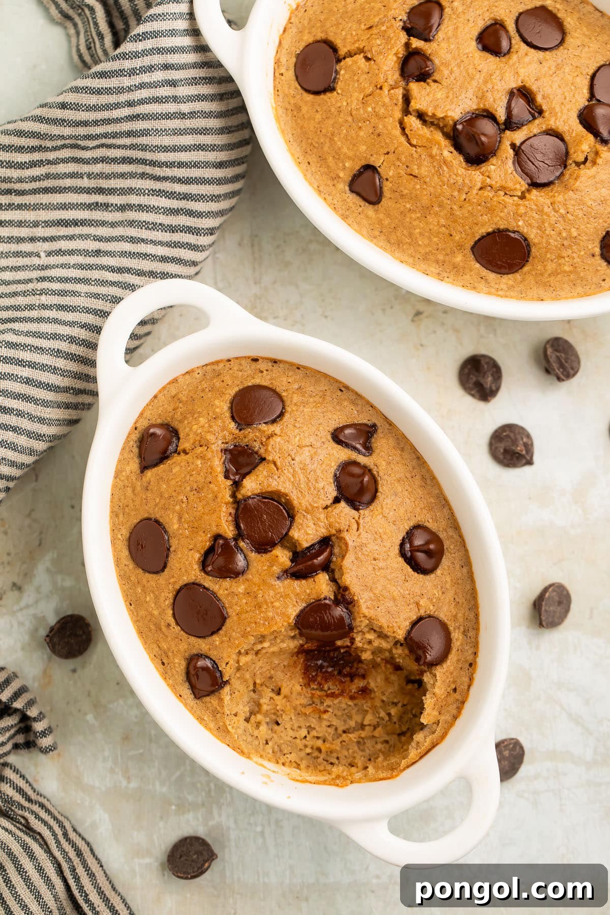 Top-down, overhead view of two oblong single-serve ramekins holding fluffy blended baked oats dotted with chocolate chips.